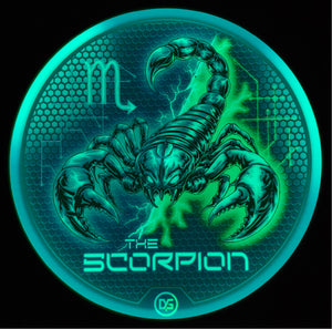 A circular graphic featuring a glowing teal and green scorpion illustration on a dark textured background, with the text 'THE SCORPION' and an 'M' symbol, set against a black backdrop.