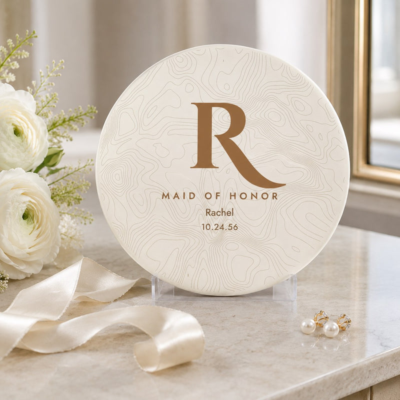 Maid of honor disc golf disc with gold topographic monogram, name and wedding date displayed beside white ranunculus