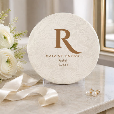 Maid of honor disc golf disc with gold topographic monogram, name and wedding date displayed beside white ranunculus